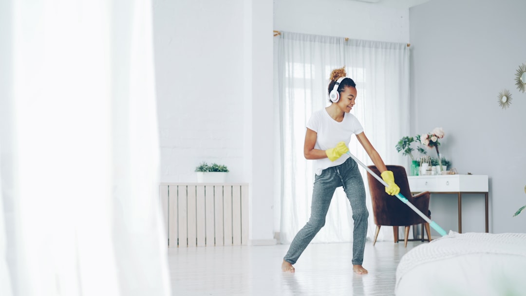Pretty African American girl cheerful maid is cleaning floor in beautiful flat with plastic mop and listening to music, singing and dancing. Routine, house and fun concept.