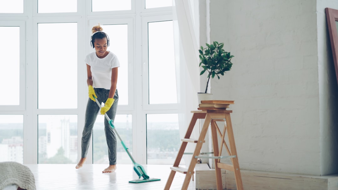 African American girl is doing housework in nice tidy flat, young woman is mopping floor and having fun listening to music, dancing and singing. Home, people and cleanliness concept.